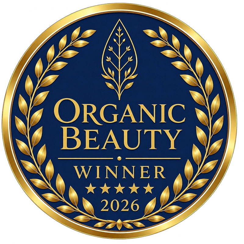 A circular organic beauty award badge with a navy blue background, gold laurel wreath, and gold text reading 'ORGANIC BEAUTY WINNER 2026' with five stars.