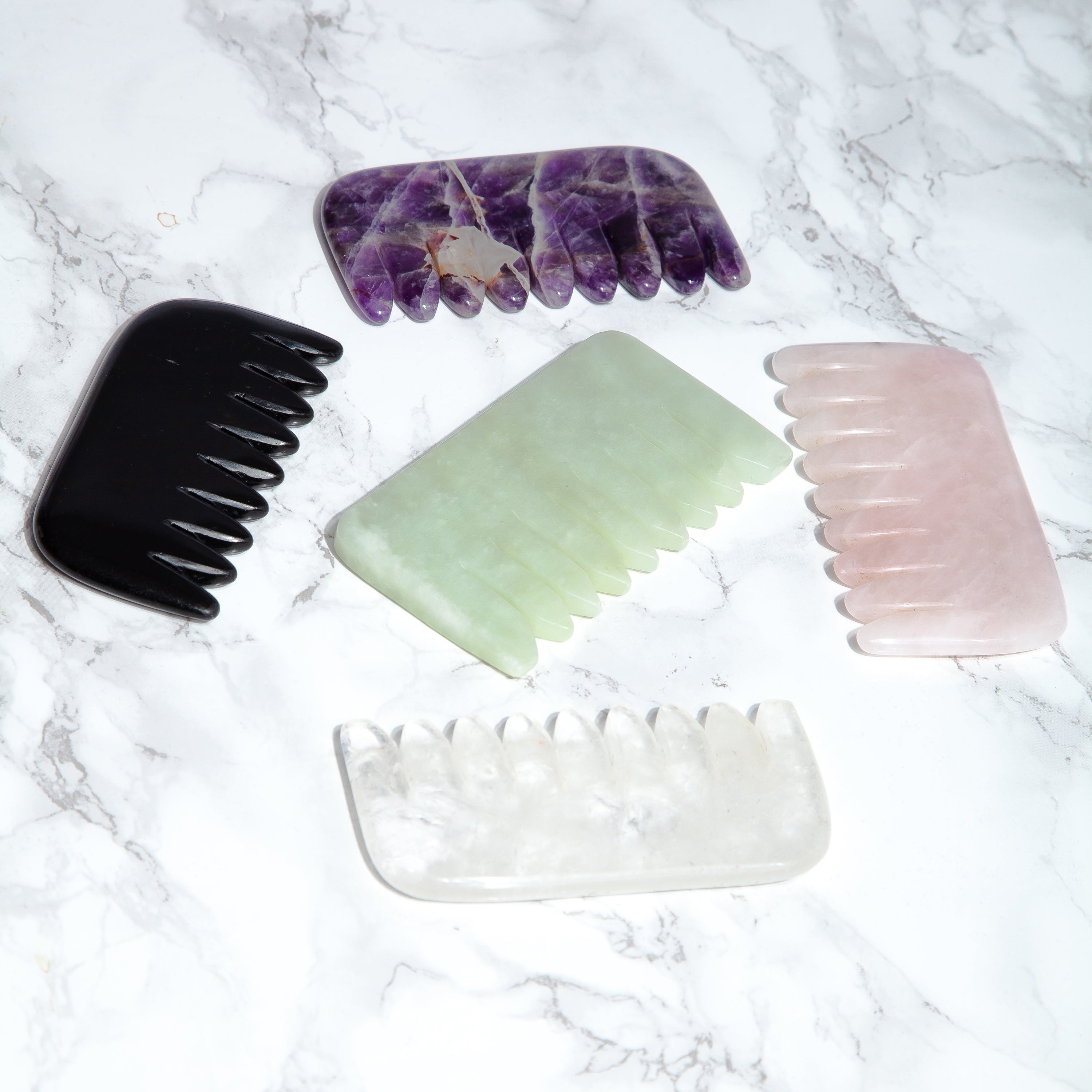 Amethyst, jade, rose quartz , black tourmaline and clear quartz crystal combs on a marble background